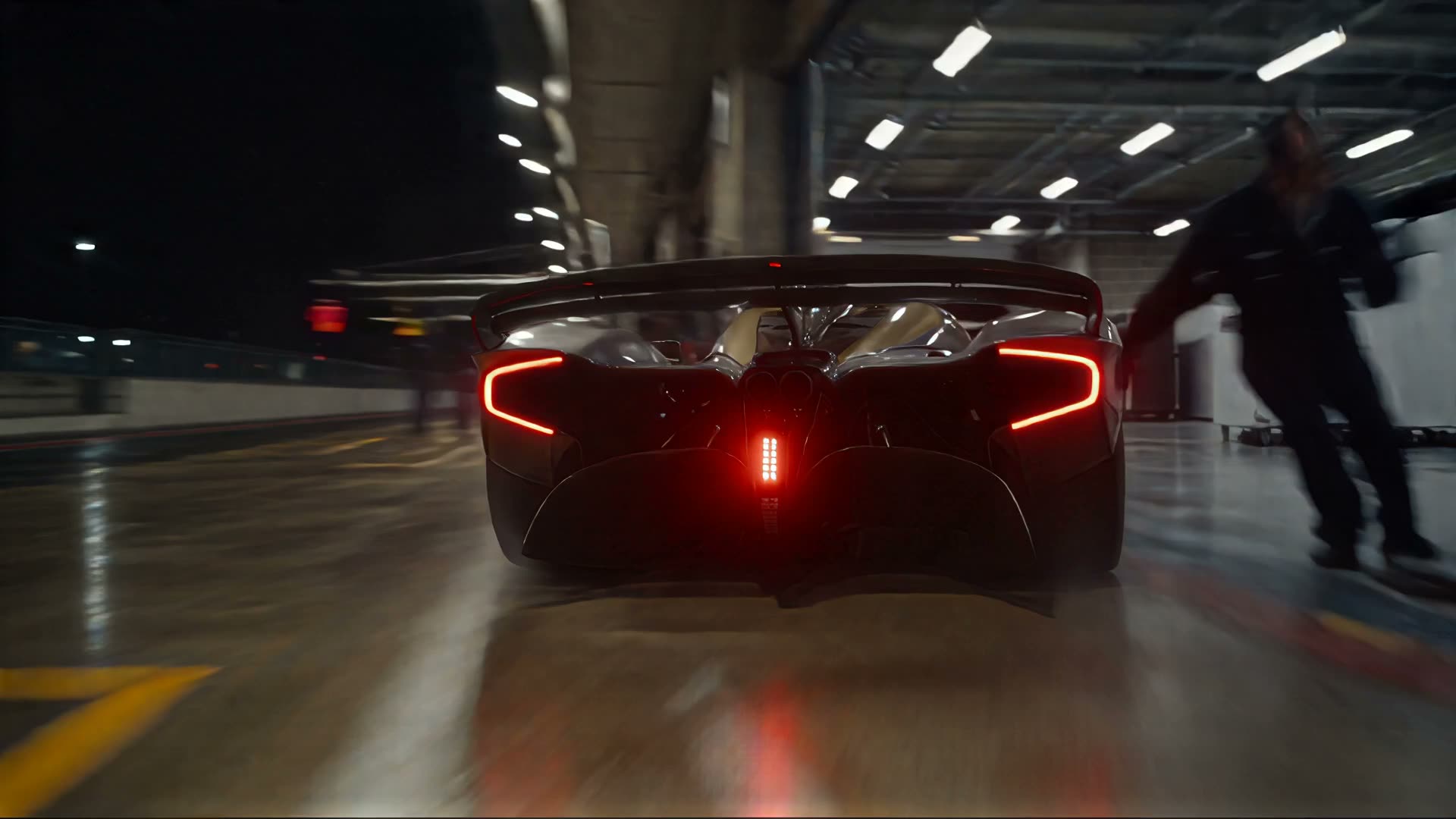 The car returns to the garage between mechanics in team kit, under the neon lights of the pit lane.