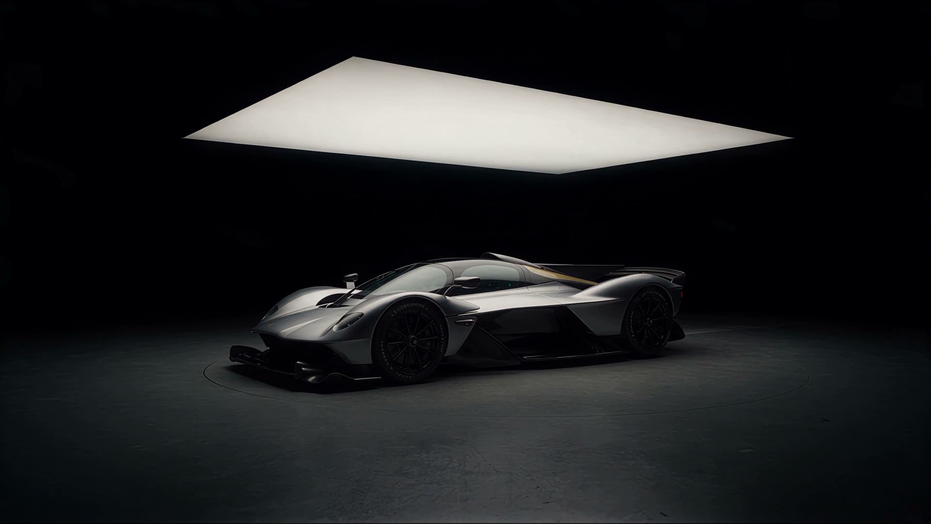 Silver hypercar standing in a black studio under a large suspended light panel.