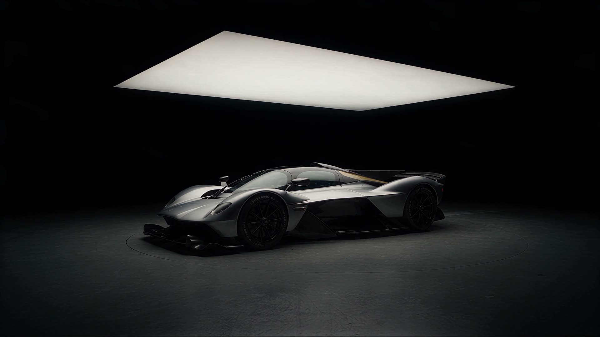Silver hypercar standing under a light panel in a black studio.