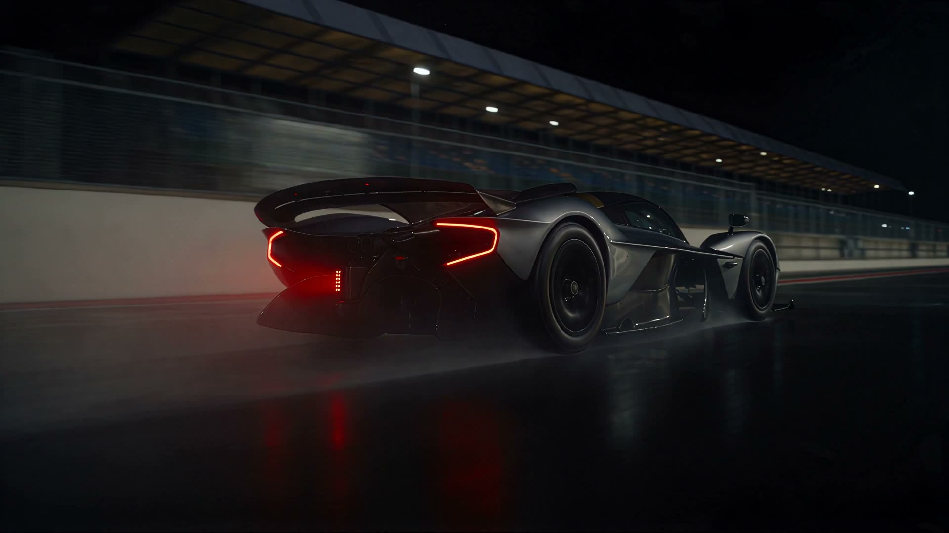 Competition prototype in the pit lane at night, seen from behind with tail lights on.